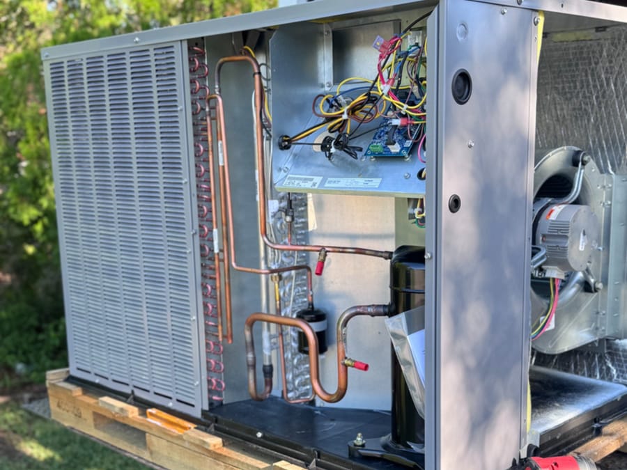 Open HVAC unit with exposed pipes and wires.